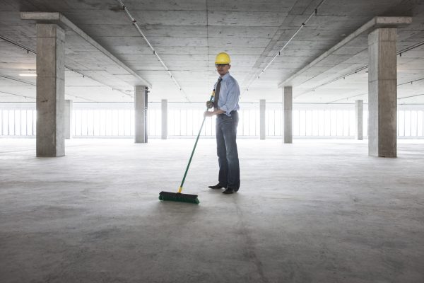 Asian businessman cleaning up with a broom in a large empty raw office space.