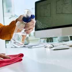 Close-up of businesswoman disinfecting her desk while working in the office.
