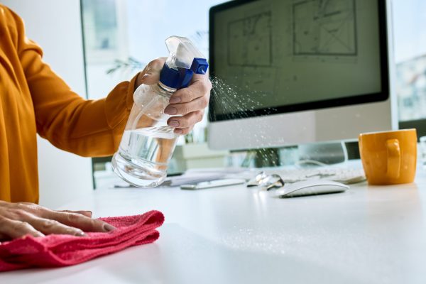 Close-up of businesswoman disinfecting her desk while working in the office.
