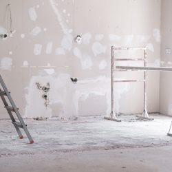 Ladder and construction equipment standing in empty room illuminated by bright sunlight shabby wall with holes and stains ready for painting renovation process in apartment
