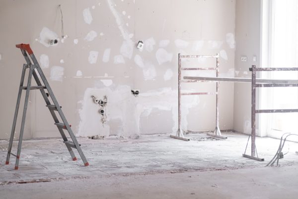 Ladder and construction equipment standing in empty room illuminated by bright sunlight shabby wall with holes and stains ready for painting renovation process in apartment