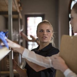 Two women with clipboard talking at shelf